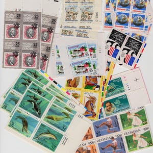 May include: A collection of vintage USA postage stamps, featuring various designs and themes. Stamps depict historical figures, Olympic athletes, animals, and scenes. The stamps are in sheets and strips, with denominations of 25 cents.