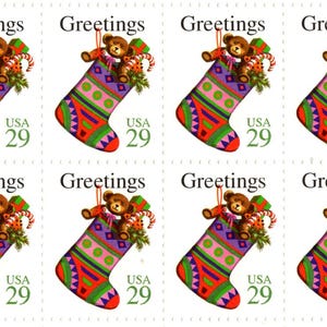 May include: A sheet of eight postage stamps, each featuring a colorful Christmas stocking with a teddy bear, candy cane, and wrapped gifts. The text 'Greetings' appears at the top, and 'USA 29' is printed in green on the lower right of each stamp.