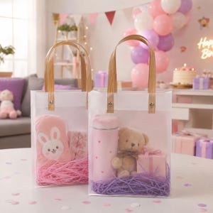 May include: Two clear plastic gift bags with light brown handles. The left bag contains a pink plush bunny pouch and pink paper filler. The right bag holds a light pink water bottle with heart patterns, a small teddy bear, and a pink gift box.