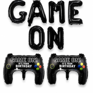 Op de afbeelding: Een set zwarte folieballonnen met de letters GAME ON en twee zwarte, controller-vormige ballonnen met de tekst GAME ON! IT'S YOUR BIRTHDAY, voorzien van kleurrijke ronde knoppen en een wit richtingskruis.