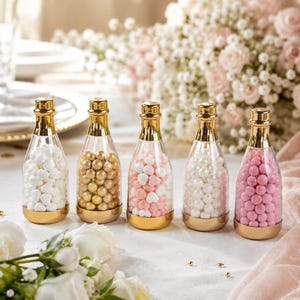 Könnte beinhalten: Fünf klare Glasflaschen mit goldfarbenen Verschlüssen und Böden, jeweils gefüllt mit kleinen Bonbons. Die Flaschen enthalten weiße herzförmige Bonbons, goldene Kugeln, eine Mischung aus weißen und rosa Herzen, weiße Perlen und rosa Kugeln.