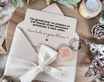 May include: A wedding proposal set featuring a cream-colored envelope tied with a frayed ribbon, a card with French text, and a wooden keychain. The keychain reads "Garçon d'honneur EN OR". The set is on a wooden tray with decorative elements.