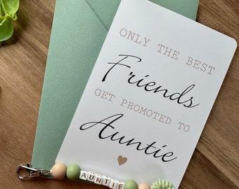 May include: A white card with the text "Only the best friends get promoted to Auntie" with a pink heart. A green and beige beaded keychain with the word "Auntie" spelled out in gold letters.