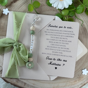 May include: A green and white beaded keychain with the word "MARRAINE" spelled out. The keychain is attached to a card with the text "Jaimerai que tu sois... MA PERSONNE DE CONFIANCE, MA SOURCE INFINIE D'AFFECTION, MA CONFIDENTE QUI GARDERA TOUS MES SECRETS, MA COMPLICE DE RIGOLADE MON ALIBI EN TOUTES CIRCONSTANCES, MA MAMAN DE SECOURS. MON &Eacute;PAULE SUR LAQUELLE M'APPUYER. MON ANGE GARDIEN POUR LA VIE... Veux-tu &ecirc;tre ma Marraine?"