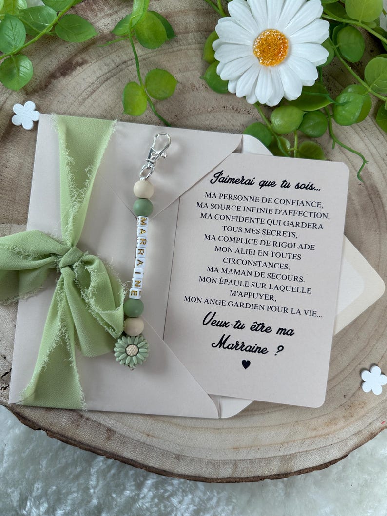 May include: A green and white beaded keychain with the word "MARRAINE" spelled out. The keychain is attached to a card with the text "Jaimerai que tu sois... MA PERSONNE DE CONFIANCE, MA SOURCE INFINIE D'AFFECTION, MA CONFIDENTE QUI GARDERA TOUS MES SECRETS, MA COMPLICE DE RIGOLADE MON ALIBI EN TOUTES CIRCONSTANCES, MA MAMAN DE SECOURS. MON &Eacute;PAULE SUR LAQUELLE M'APPUYER. MON ANGE GARDIEN POUR LA VIE... Veux-tu &ecirc;tre ma Marraine?"