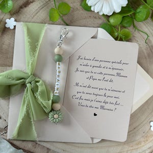 May include: A white envelope with a green ribbon and a green and white beaded keychain with the word "MARRAINE" spelled out on it. The envelope has a handwritten note inside that reads "J'ai besoin d'une personne sp&eacute;ciale pour m'aider &agrave; grandir et &agrave; m'&eacute;panouir. Je sais que tu es cette personne, Maman et Papa me l'ont dit. Ils m'ont dit aussi que tu m'aimeras et que tu seras toujours l&agrave; pour moi. C'est fou mais je t'aime d&eacute;j&agrave; tr&egrave;s fort.... Veux-tu &ecirc;tre ma Marraine?"