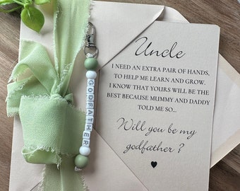 May include: A light brown card with green ribbon and a beaded keychain that says "Godfather". The card says "Uncle, I need an extra pair of hands to help me learn and grow. I know that yours will be the best because Mummy and Daddy told me so... Will you be my godfather?"