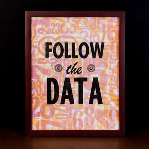 Könnte beinhalten: Ein gerahmter Kunstdruck mit dem Text "FOLLOW the DATA" in schwarzer Schrift. Der Hintergrund besteht aus orangefarbenen und rosa Zahlen. Der Rahmen ist dunkelbraun.