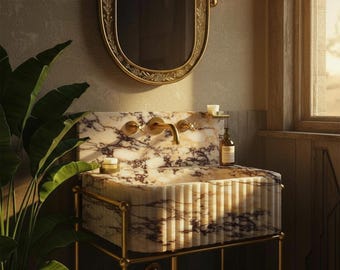 May include: A marble bathroom sink with gold taps and a matching mirror. The sink is supported by a gold metal frame. The room features a window and a green plant, creating a luxurious and elegant atmosphere.
