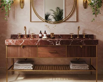 May include: A modern bathroom vanity with a red marble countertop and gold fixtures. The vanity has two sinks, a central drawer, and two ribbed cabinet doors. A gold-framed mirror hangs above, with hanging plants and sconces on the wall.