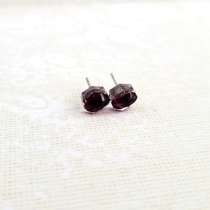 May include: A pair of small, square-shaped earrings with a dark purple gemstone. The earrings are made of silver and have a simple, elegant design.