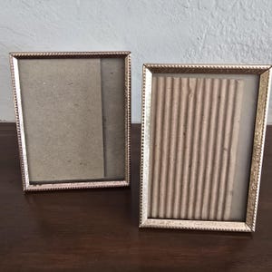 May include: Two rectangular picture frames with metallic gold-toned borders featuring a beaded edge texture. The left frame contains a smooth tan backing, while the right frame holds a piece of vertically corrugated tan cardboard inside the glass.