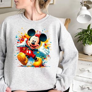 a woman sitting on a bed wearing a mickey mouse sweatshirt