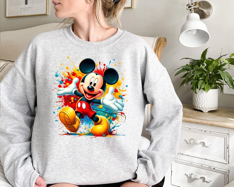 a woman sitting on a bed wearing a mickey mouse sweatshirt