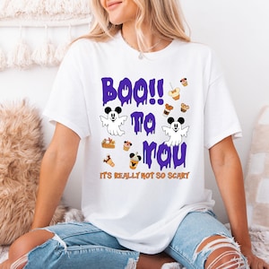 Puede incluir: Camiseta blanca con un diseño temático de Halloween. El diseño presenta el texto "Boo to You" en morado goteando, junto con ilustraciones de fantasmas y comida de dibujos animados. La frase "It's Really Not So Scary" está impresa debajo.