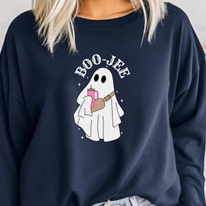 May include: A navy blue sweatshirt with a white ghost holding a pink drink and a brown bag. The text "BOO-JEE" is written in white above the ghost.