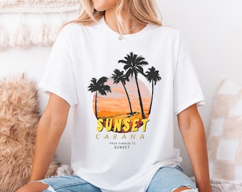 May include: White t-shirt featuring a sunset design with palm trees and the text "Sunset Cabana". The graphic includes a yellow and orange sunset with black palm tree silhouettes. The text "From Sunrise to Sunset" is also included.