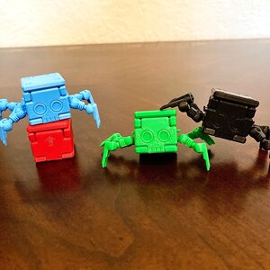 May include: Three small, colorful robots with articulated legs and a block-like body. The robots are blue, green, and black.