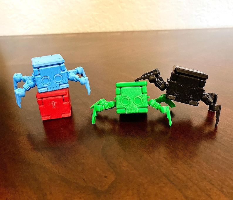 May include: Three small, colorful robots with articulated legs and a block-like body. The robots are blue, green, and black.
