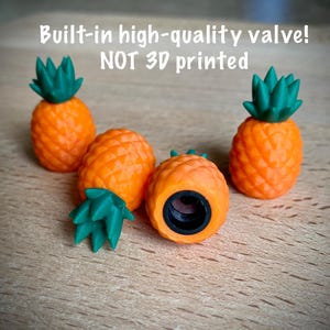 May include: Four pineapple-shaped valve caps with orange bodies and green tops. The text "Built-in high-quality valve! NOT 3D printed" is visible. One cap is positioned to show the black threaded interior, while the others stand upright.