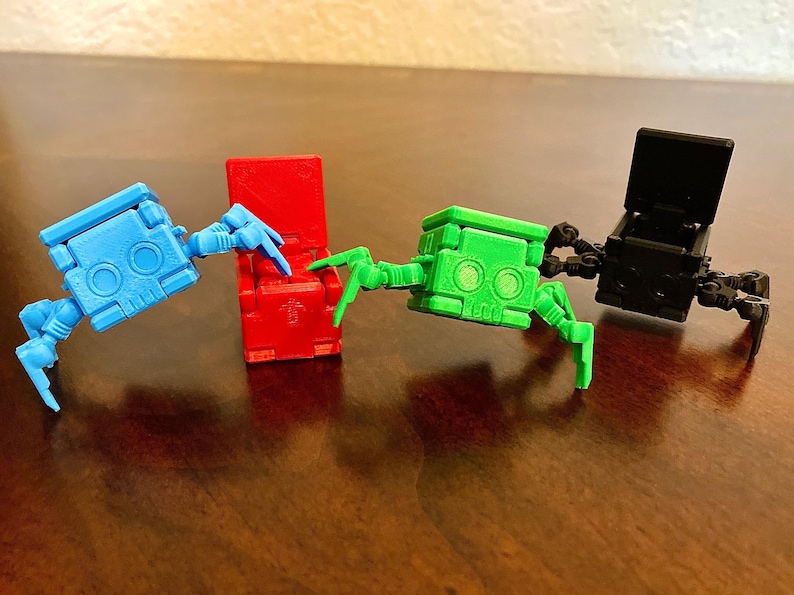 May include: Three small, colorful, articulated robot toys with spindly legs. The robots are red, green, and black. The red robot is sitting down, the green robot is standing with its legs spread out, and the black robot is standing with its legs together.