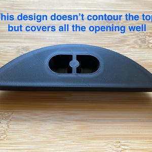 May include: A black plastic 3D printed object with two holes in the center. The object is shaped like a half-circle and is sitting on a wooden surface.