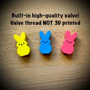 May include: Three bunny-shaped figures in yellow, blue, and pink with black dot eyes and noses. Text reads: Built-in high-quality valve! Valve thread NOT 3D printed. These small, solid-colored items feature a smooth finish and distinct ears.