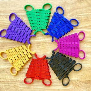 May include: Seven colorful plastic scissor-like tools with interlocking pieces. Each tool is a different color: purple, yellow, red, black, pink, blue, and green.