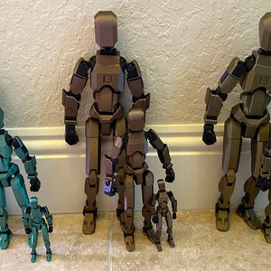 May include: Five articulated plastic figures in different sizes, ranging from small to large. The figures are all in shades of green and brown, with the largest figure being a dark green color. The figures are all standing upright and have a humanoid shape.