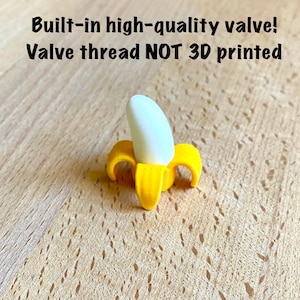 May include: A small yellow and white banana-shaped valve component with text above it reading Built-in high-quality valve! Valve thread NOT 3D printed. The object features a bright yellow peel base and a smooth white banana fruit top.