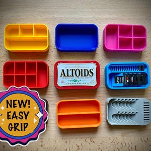 May include: A collection of colorful, 3D-printed storage containers and organizers. Includes yellow, blue, pink, red, orange, and gray containers, some with compartments. An Altoids tin and a "NEW! EASY GRIP" sticker are also present.
