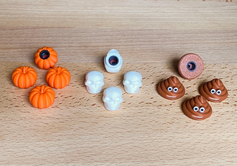 May include: A collection of small decorative charms including four orange pumpkins, four white skulls, and three brown smiling poop emojis with googly eyes. Each charm features a circular attachment point on the back for use as a shoe accessory.