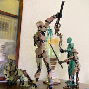 May include: Five articulated action figures, some with weapons, posed in a dynamic scene. The figures are made of plastic and have a metallic finish in shades of brown, green, and silver. The figures are standing on a wooden surface.