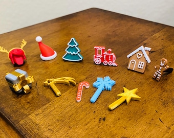 May include: A collection of 11 Christmas-themed ornaments, including a red Santa hat, a green Christmas tree, a red and white train, a gingerbread house, a gingerbread man, a gold star, a gold star with a red candy cane, a gold star with a blue snowflake, a gold star with a silver gift box, a gold star with a red and white candy cane, and a gold star with a red and white candy cane.