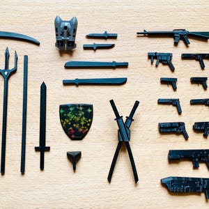 May include: A collection of black weapons and tools, including a scythe, a trident, a sword, a shield, a pair of katanas, and several guns. The shield has a colorful design with a rainbow pattern.