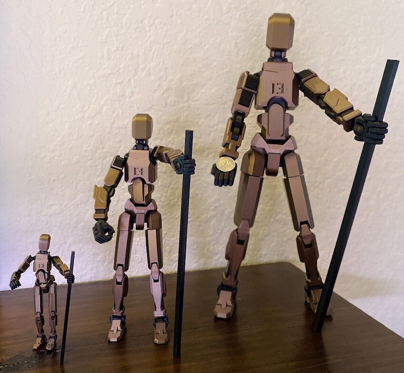 May include: Three articulated action figures made of brown plastic. The figures are standing on a wooden surface. The figures are holding black sticks. The tallest figure is holding a stick in its right hand and a coin in its left hand. The middle figure is holding a stick in its right hand. The smallest figure is holding a stick in its left hand.