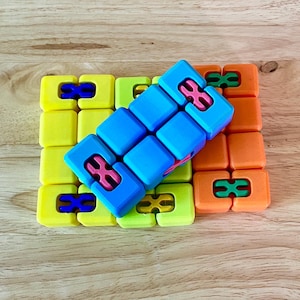 May include: A blue and pink puzzle toy with a square shape. The toy is made of plastic and has a variety of colors. The toy is sitting on top of a yellow and orange puzzle mat.