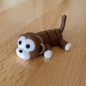 May include: A brown and white segmented monkey figurine with a curled tail. The monkey is lying on its side with its head resting on the surface.