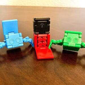 May include: Three small, articulated robot toys. One is blue, one is green, and one is red and black. The robots have a skull-like face and articulated legs.