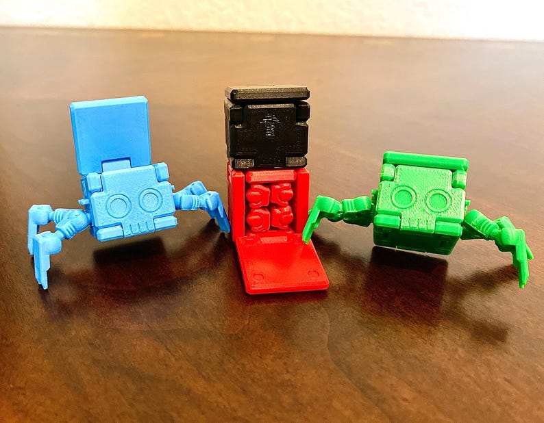 May include: Three small, articulated robot toys. One is blue, one is green, and one is red and black. The robots have a skull-like face and articulated legs.