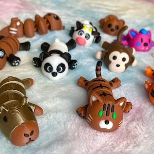 Op de afbeelding: Een verzameling kleurrijke dierenbeeldjes, waaronder een panda, een tijger, een aap en een muis. De beeldjes zijn gemaakt van een glad materiaal en zijn gerangschikt op een zacht, patroonrijk oppervlak. Elk dier heeft unieke details.