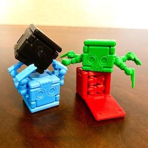 May include: Two small, colorful robots made of plastic blocks. One robot is blue with black arms and a black head. The other robot is green with red legs and red arms.