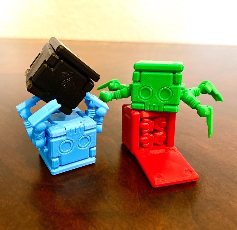 May include: Two small, colorful robots made of plastic blocks. One robot is blue with black arms and a black head. The other robot is green with red legs and red arms.