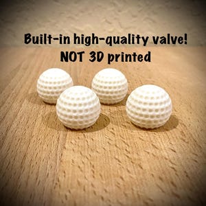 Könnte beinhalten: Vier weiße Golfbälle mit vertieften Oberflächen liegen auf einer Holzoberfläche. Der Text "Built-in high-quality valve! NOT 3D printed" ist über den Golfbällen zu sehen.