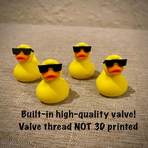 May include: Four yellow rubber ducks with orange beaks, each wearing black sunglasses. Text on the image reads: Built-in high-quality valve! Valve thread NOT 3D printed. These small figures are arranged in a group on a textured surface.