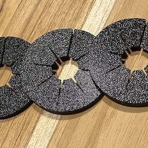 May include: Three black, round, segmented, plastic rings with a hole in the center. The rings are connected together.