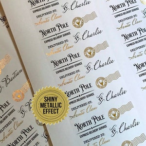 May include: Sheets of white paper with gold foil labels. Each label reads "North Pole Express Delivery Service, Delivered by Santa Claus" and "To Charlie." A gold foil seal with a reindeer is also present. The labels have a shiny metallic effect.