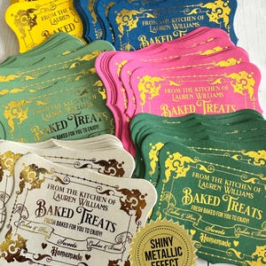 May include: A collection of colorful, decorative labels with gold foil accents. The labels feature the text "Baked Treats" and "From the Kitchen of Lauren Williams." The labels are in various colors, including yellow, blue, pink, green, and cream.