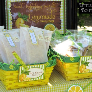 May include: Two yellow wicker baskets filled with treats for sale. The basket on the left contains Rice Krispie treats wrapped in white paper bags with "50 cents" labels. The basket on the right contains chocolate chip cookies in clear plastic bags with "25 cents" labels. Both baskets have green and yellow striped labels with the names of the treats.