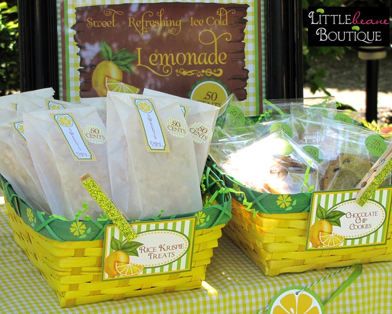May include: Two yellow wicker baskets filled with treats for sale. The basket on the left contains Rice Krispie treats wrapped in white paper bags with "50 cents" labels. The basket on the right contains chocolate chip cookies in clear plastic bags with "25 cents" labels. Both baskets have green and yellow striped labels with the names of the treats.